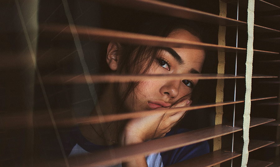 sad girl looking through blinds